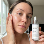 Woman holding a bottle of Liviera skincare product near her face.