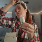 Woman applying cream to her face with a brush, wearing a plaid shirt indoors.