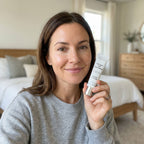 Woman holding a skincare product in a bedroom setting