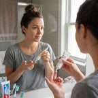 Woman applying cream to her arm in front of a mirror