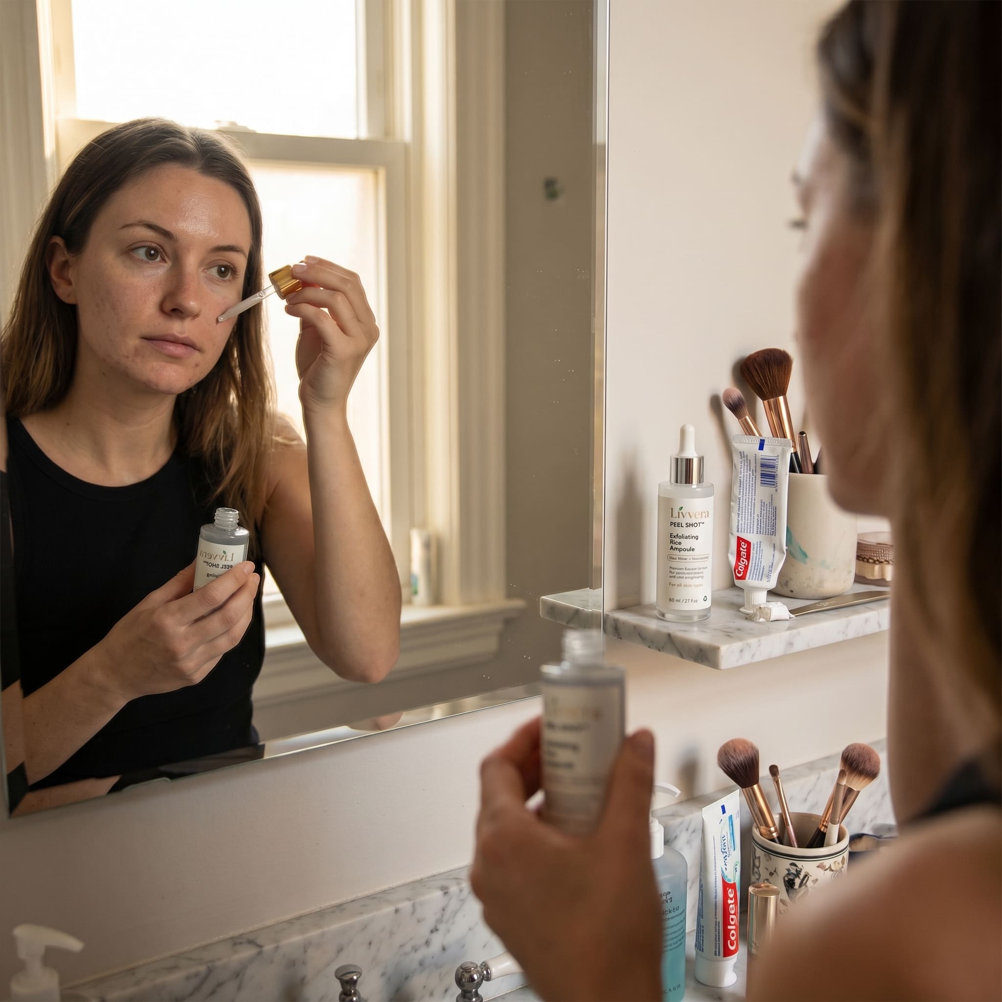 Woman applying skincare product in front of a bathroom mirror with various skincare items on the counter.
