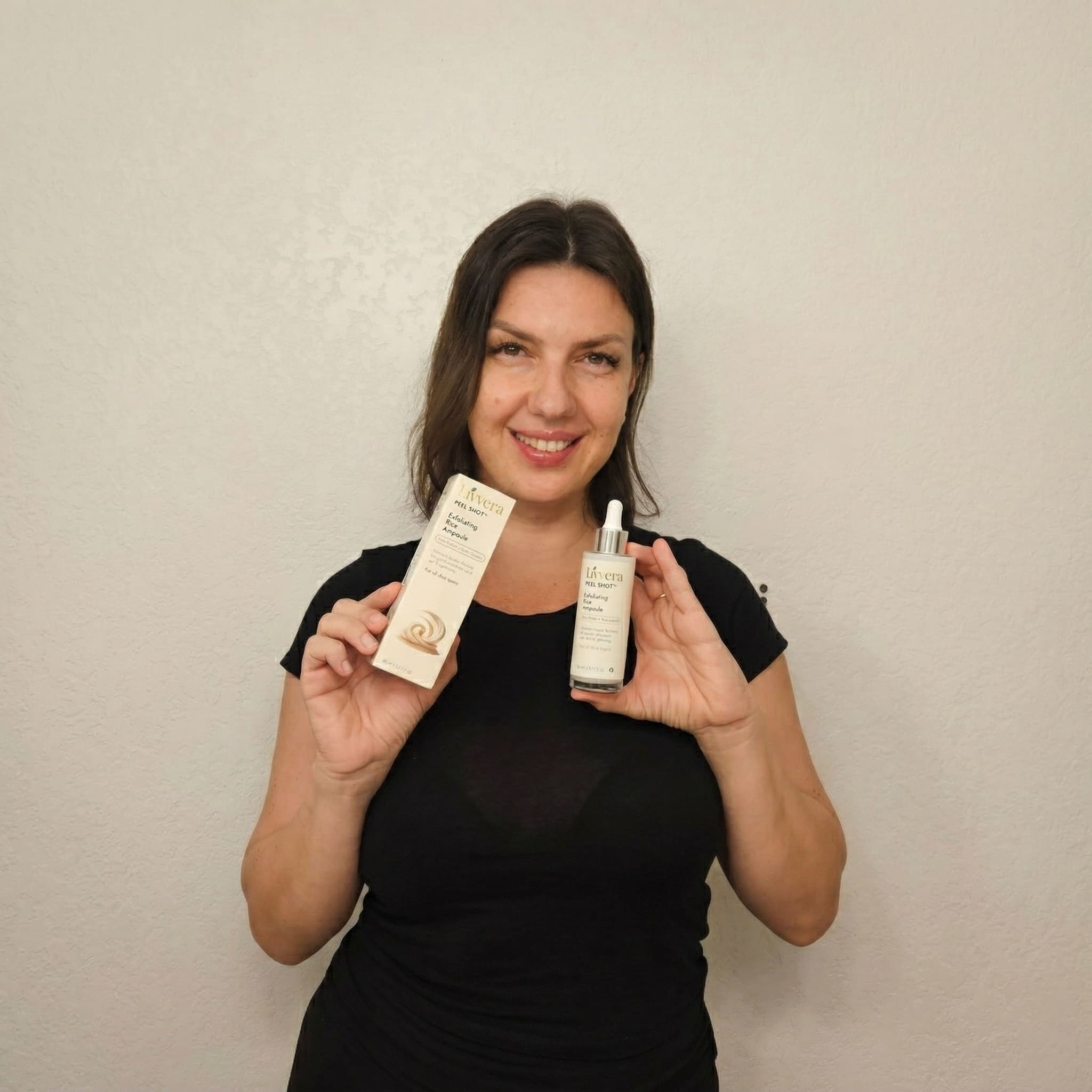 Woman holding two skincare products against a plain background