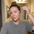 Woman applying a skincare product to her face in front of a mirror.