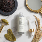 Livvera Exfoliating Black Rice Ampoule bottle on a marble surface with a gold roller, bowl of black rice, and decorative mirror.