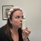 Woman holding a skincare bottle with a neutral background